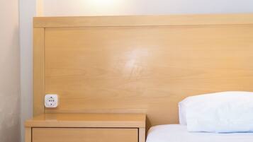 Una cama bien hecha con un cojín blanco y una mesita de noche de madera con cajón y lámpara.