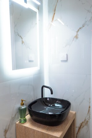 Une salle de bain avec un lavabo noir, un distributeur de savon vert et un miroir.