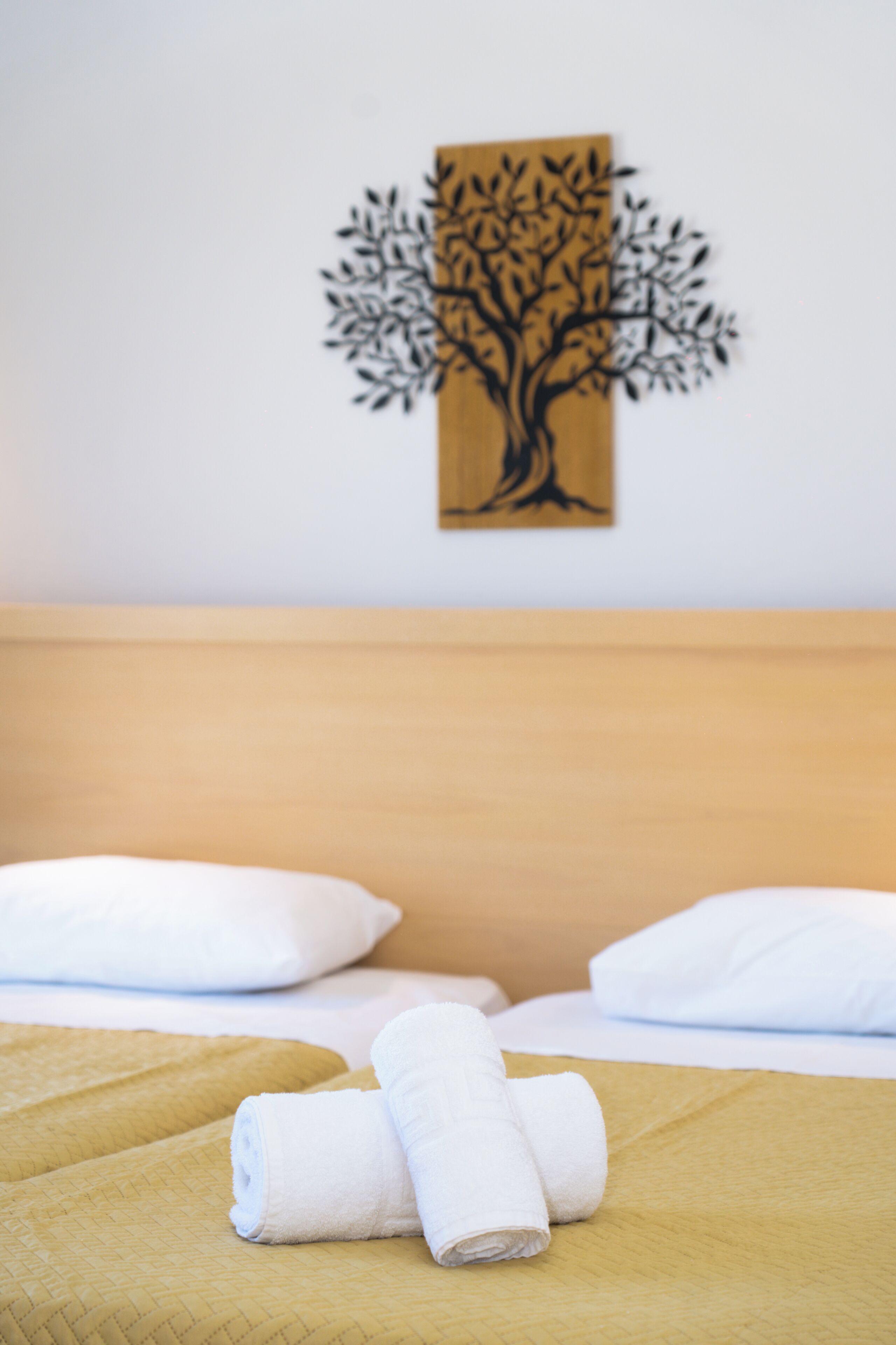A hotel room with a bed, two white pillows, a yellow bedspread, and a wall art of a tree.