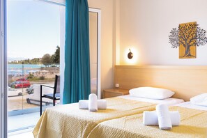 Une chambre d’hôtel avec deux lits, une vue sur la plage, une décoration murale représentant un arbre et une table de chevet avec une lampe.
