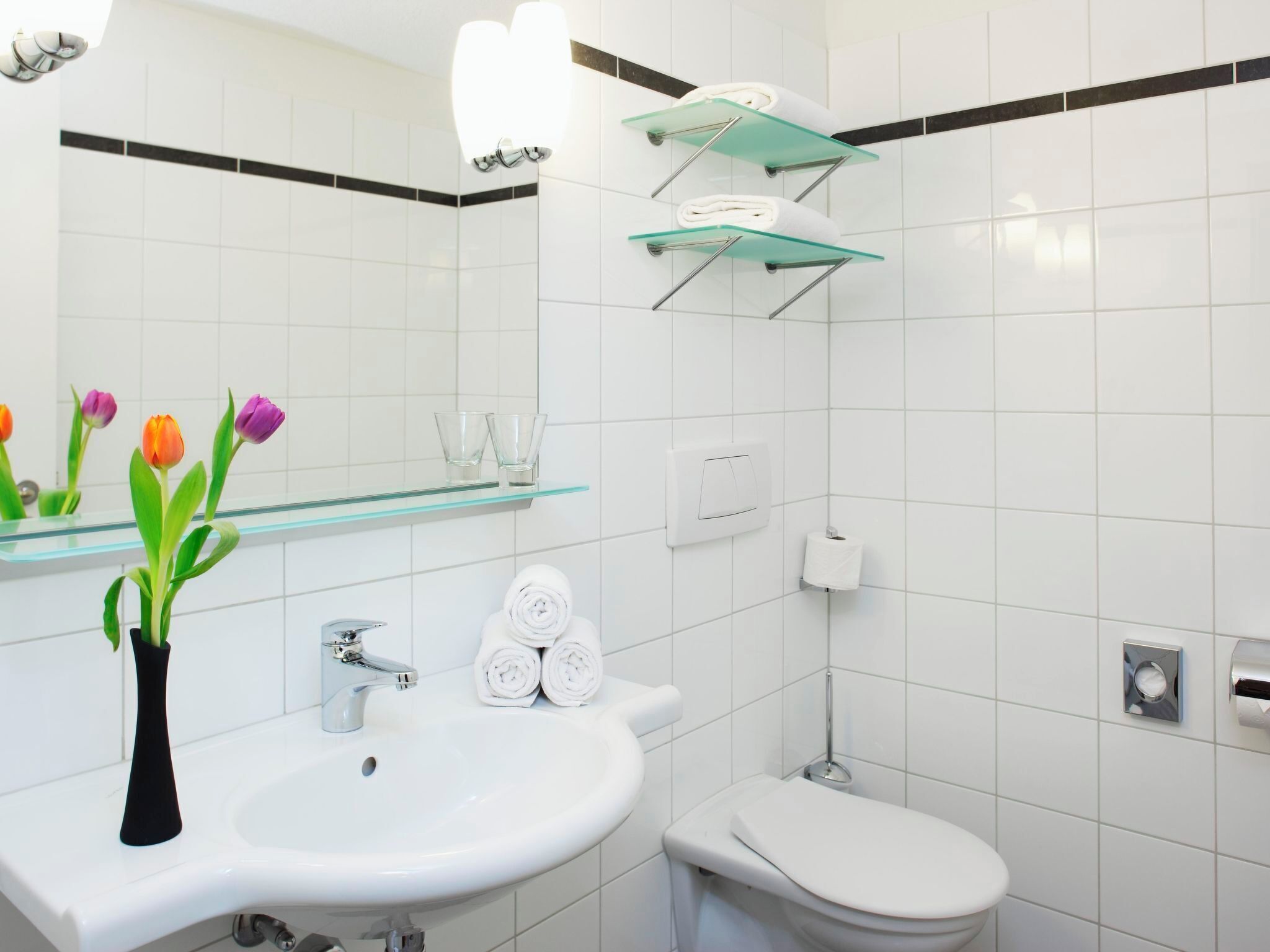 Een moderne badkamer met een witte wastafel, een toilet en een glazen plank boven het toilet.