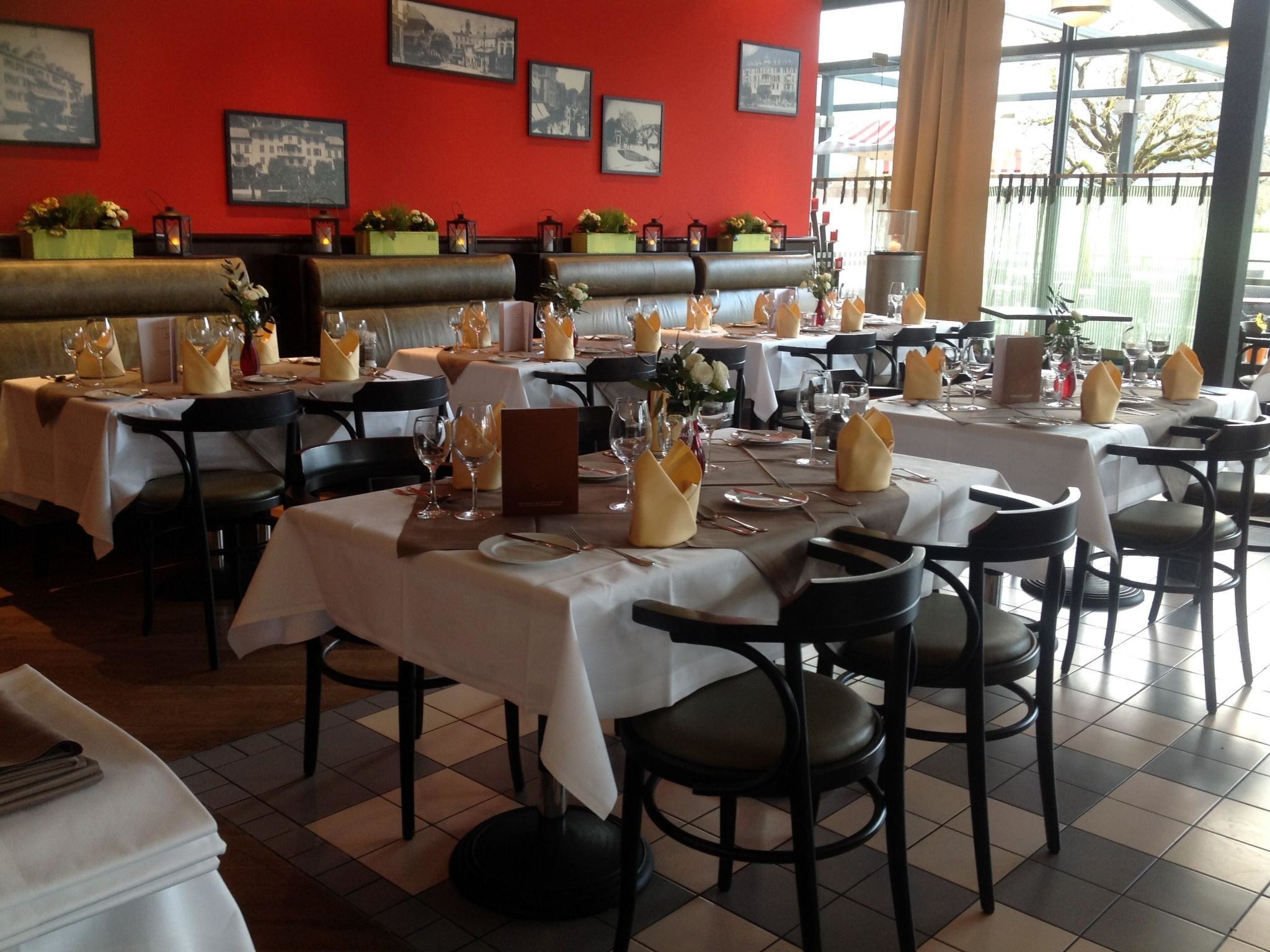 Un restaurant avec des tables dressées, des chaises et un mur rouge orné de tableaux.