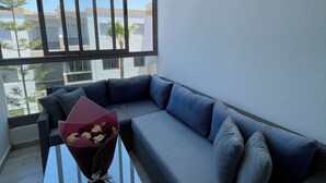 A balcony with a sofa, a glass table, and a wall-mounted light fixture. - Design Apt @ Blanca Beach: Private Beach & Pool (Sidi Rahal)