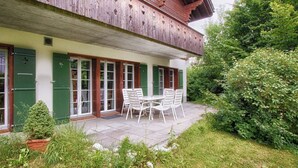 Ein Holzhaus mit Balkon, einer überdachten Terrasse mit Tisch und Stühlen und einem Garten.
