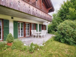 A wooden building with a balcony, a covered patio with a table and chairs, and a garden area. - CityChalet Appartement/Fewo Alpenrose**** by Interhome (Interlaken)