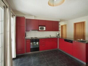 A modern kitchen with red cabinets, a black oven, and a microwave. - CityChalet Appartement/Fewo Alpenrose**** by Interhome (Interlaken)