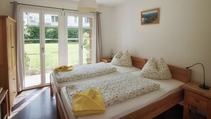 Ein Schlafzimmer mit einem Doppelbett, einem Nachttisch, einer Lampe und Blick auf einen Garten durch eine Schiebetür.