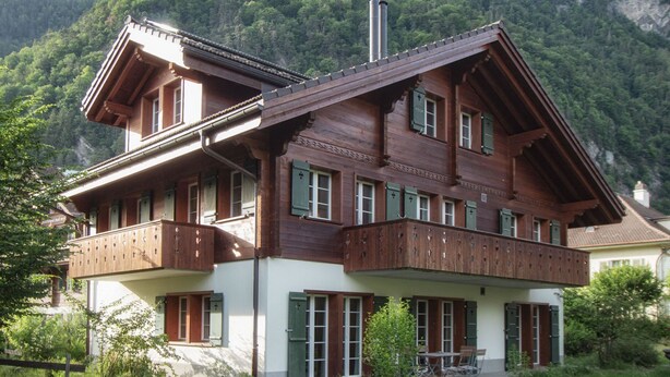 Ein mehrstöckiges Holzchalet mit Balkonen vor einer Bergkulisse.