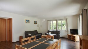 Ein Wohnzimmer mit einem Holzespeisetisch, zwei Sofas, einem Fernseher und einem Fenster mit Vorhängen.