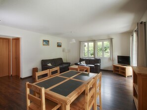 A living room with a wooden dining table, two sofas, a TV, and a window with curtains. - CityChalet Appartement/Fewo Alpenrose**** by Interhome (Interlaken)