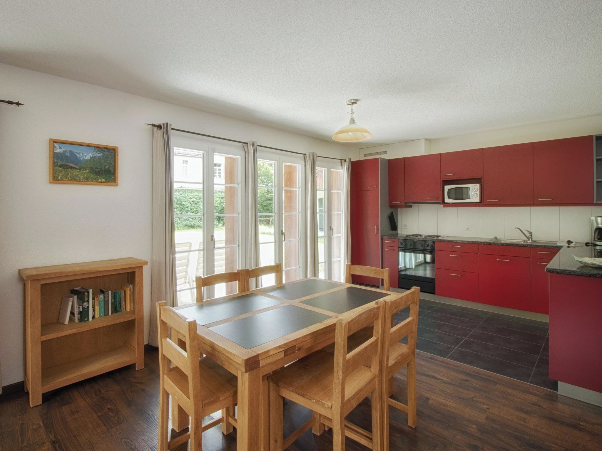 Zona pranzo con tavolo e sedie in legno, una libreria e vista panoramica attraverso ampie finestre.