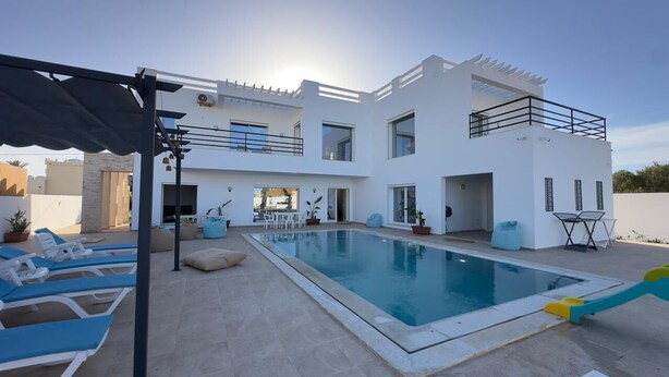 Una casa moderna de dos pisos con piscina, mobiliario exterior y una pérgola.