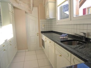 A kitchen with white cabinets, a black countertop, and a window above the sink. - Adlerhorst Leukerbad # 6-bed apartment, Dusche oder Bad, WC by Interhome (Leukerbad)