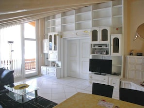 A living room with a TV, white cabinets, a dining table, and a balcony. - Adlerhorst Leukerbad # 6-bed apartment, Dusche oder Bad, WC by Interhome (Leukerbad)