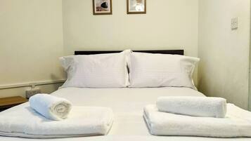A hotel room with a bed, two pillows, two bedside tables with towels, and two framed pictures on the wall.