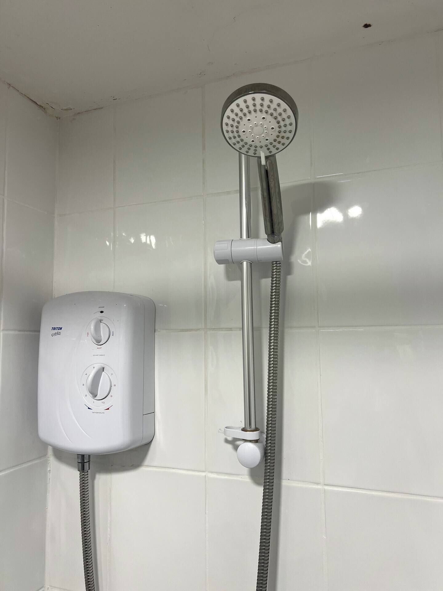 A white shower with a handheld showerhead and a wall-mounted control panel.