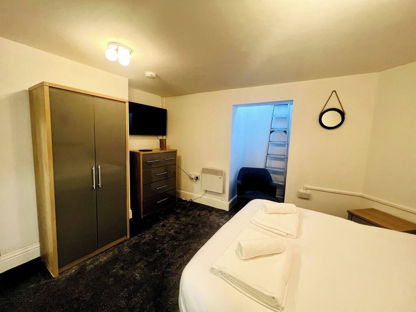 Une chambre d’hôtel dotée d’une grande armoire, d’un téléviseur à écran plat, d’un bureau avec une chaise et d’un lit avec des serviettes.