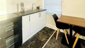 Une cuisine compacte avec des meubles blancs, un plan de travail noir, un four encastré et un coin repas comprenant une table et des chaises.