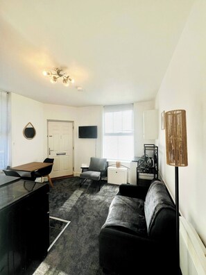 A compact living space with a kitchenette, a sofa, a dining table, and a TV mounted on the wall.