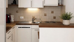 Una cocina compacta con armarios blancos, lavavajillas integrado y salpicadero de azulejos.