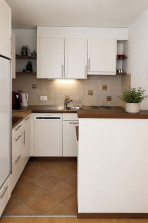 A compact kitchen with white cabinetry, a built-in dishwasher, and a tiled backsplash. - Majesta Leukerbad # 6-bed apartment, Dusche und Bad, WC by Interhome (Leukerbad)