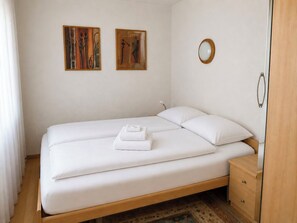 A single-bed room with a wooden frame, white bedding, a small bedside table, a nightstand, a wooden wardrobe, and two paintings on the wall. - Majesta Leukerbad # 6-bed apartment, Dusche und Bad, WC by Interhome (Leukerbad)