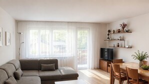 Una sala moderna con un sofá seccional, una mesa de comedor con sillas, un televisor de pantalla plana y una cocina con gabinetes de madera y encimera.