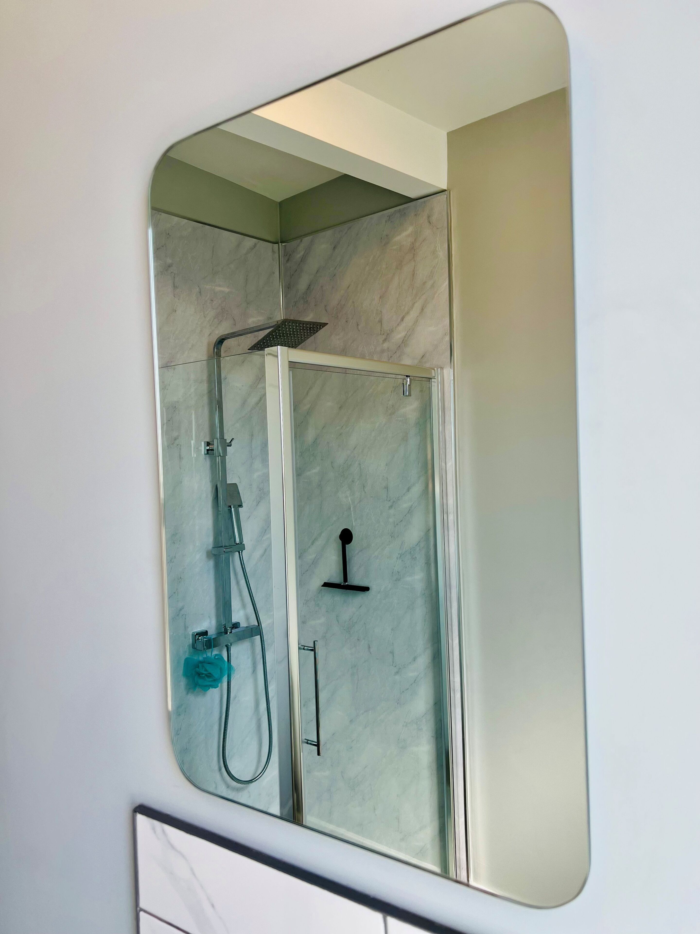 Ein modernes Badezimmer mit einer gläsernen Duschkabine, einer Handbrause und einem am Wand montierten Wasserhahn.