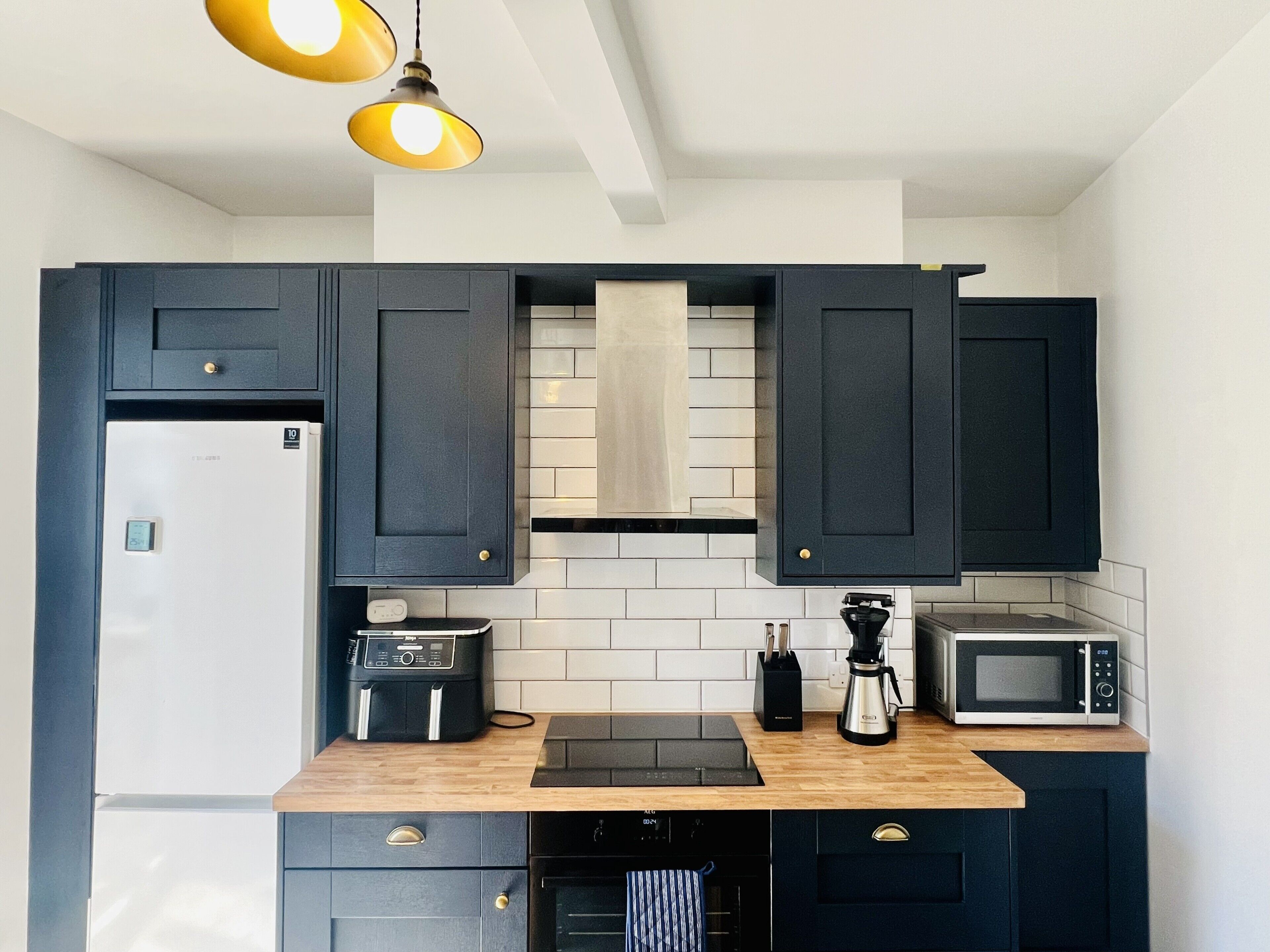 A modern kitchen with dark cabinetry, a refrigerator, a coffee maker, and a microwave.