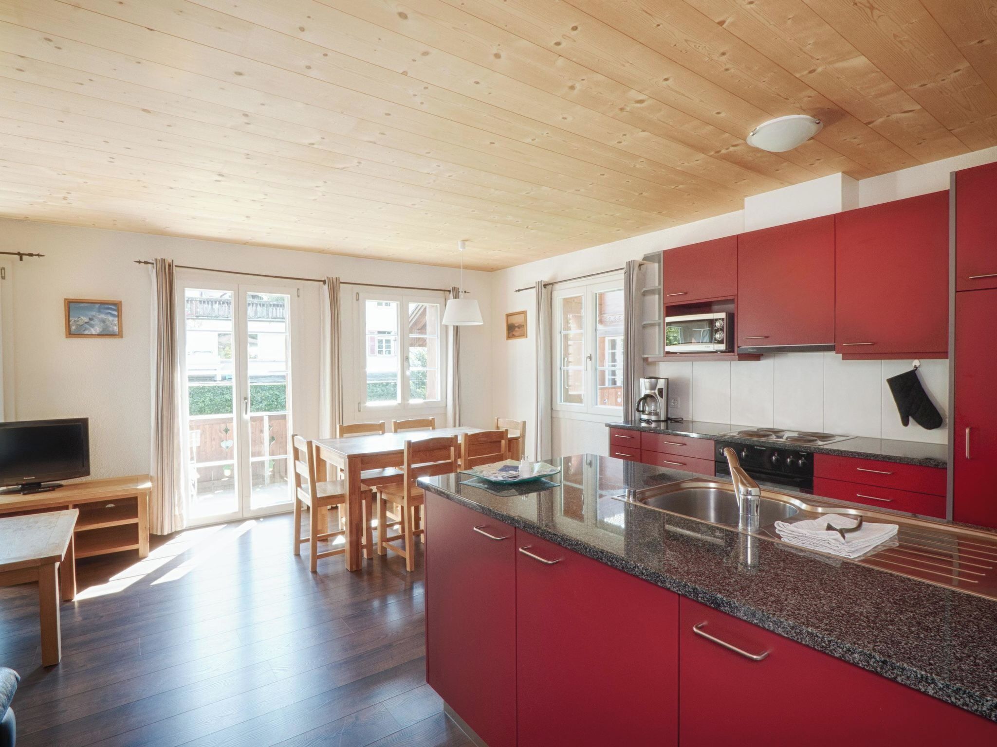 Una cocina moderna con armarios rojos, encimera de granito y comedor con mobiliario de madera.