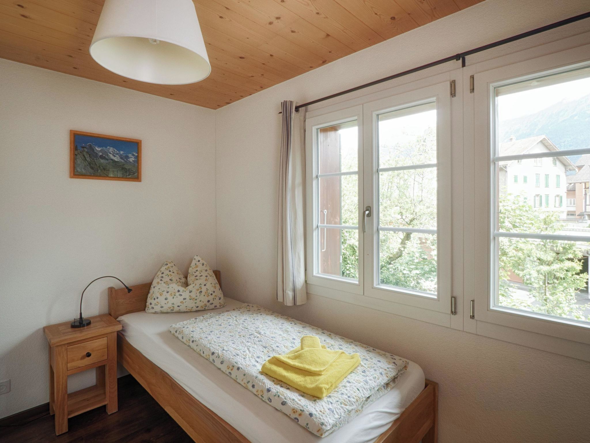 Une chambre à coucher avec un lit en bois, une table de chevet, une lampe, une fenêtre avec des rideaux et un tableau au mur.