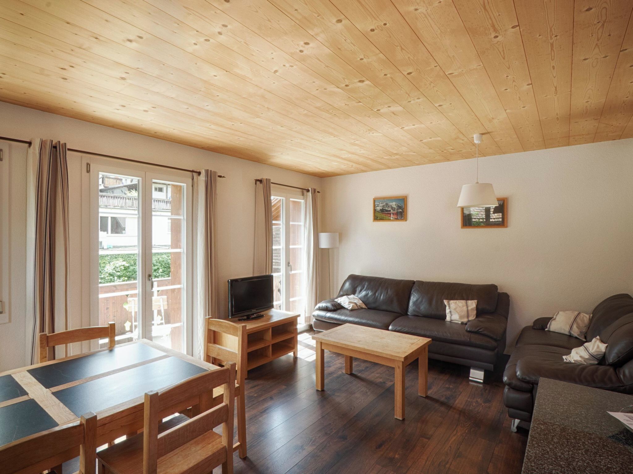 Un salon chaleureux avec un plafond en bois, un canapé, un téléviseur et un coin repas comprenant une table et des chaises.