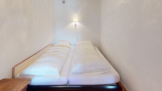 Een kleine kamer met een bed, een nachtkastje en een wandlamp.