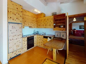 A compact kitchen with wooden cabinetry, a built-in oven, and a dining area with a bench. - Apartment Tinus by Interhome (St. Moritz)