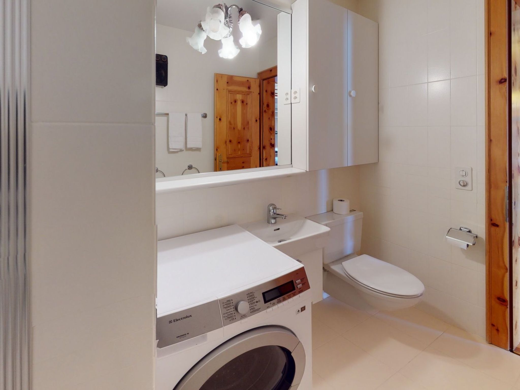 A compact bathroom with a washing machine, a toilet, and a sink.