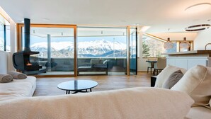 Ett modernt vardagsrum med en soffa, ett soffbord och utsikt över snöklädda berg genom stora glasdörrar.