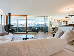 A modern living room with a sofa, a coffee table, and a view of snow-capped mountains through large glass doors. - Apartment Mira Lej by Interhome (St. Moritz)