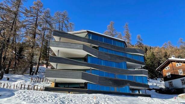 En byggnad med flera våningar och en modern arkitektonisk design, som kännetecknas av en kombination av glas och mörkfärgade paneler.