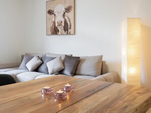 A wooden table with three pink candle holders, a grey sofa with multiple cushions, and a wall-mounted painting of a cow. - Apartment Troja Appartement/Fewo 4-Bettwohnung by Interhome (Interlaken)