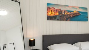 Une chambre à coucher avec un lit, une table de chevet avec une lampe, un miroir et un tableau représentant une ville côtière.