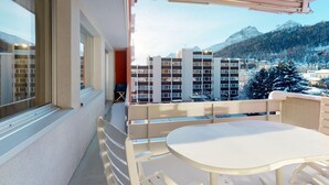 Ein Balkon mit Tisch und Stühlen, mit Blick auf einen verschneiten Berg und Gebäude.