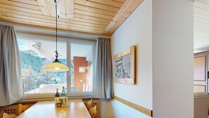 Ein Essbereich mit Holztisch, Stühlen, einer Pendelleuchte, einem Fenster mit Vorhängen und einem gerahmten Bild an der Wand.