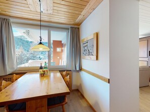 A dining area with a wooden table, chairs, a hanging light fixture, a window with curtains, and a framed picture on the wall. - Apartment Skyline 307 by Interhome (St. Moritz)
