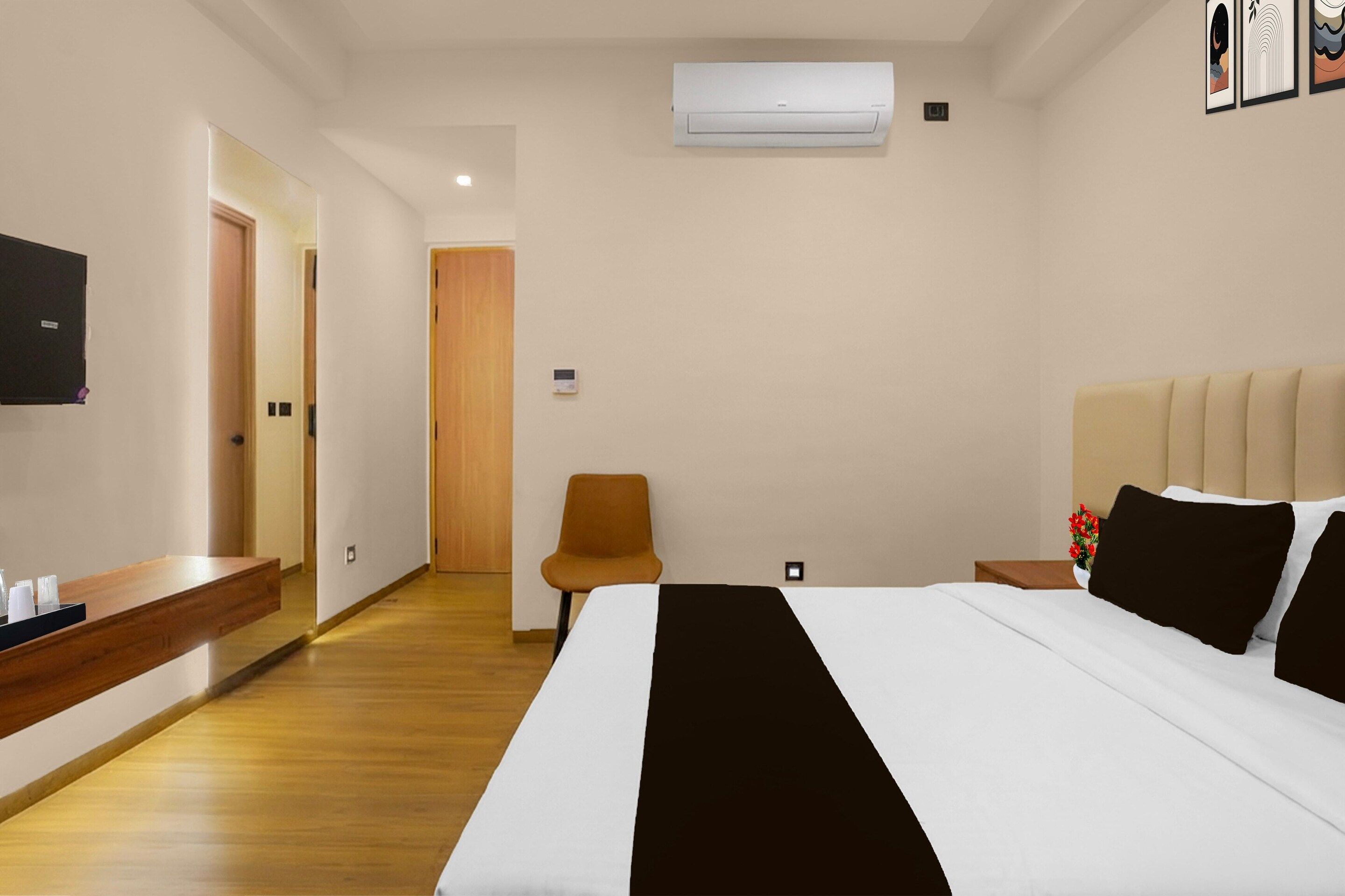 Et hotelværelse med seng, natbord, stol og en aircondition.