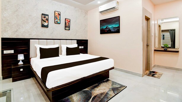 A modern hotel room with a large bed, a nightstand, a wall-mounted air conditioner, and a door leading to another room.