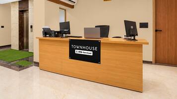 En receptionsdisk med en skylt som visar texten ”TOWNHOUSE OYO-Serviced” i en modern interiör med ett träpanelat tak och ett marmorgolv.