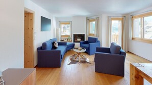 Una sala de estar moderna con chimenea, sofás azules, una mesa de centro y ventanas amplias.