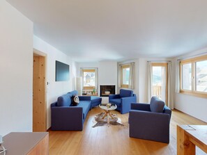 Ein modernes Wohnzimmer mit Kamin, blauen Sofas, einem Couchtisch und großen Fenstern.
