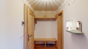 Un pasillo con puertas de madera, un banco, un perchero y un estante pequeño con una lámpara.