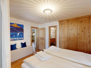 Une chambre à coucher avec un lit, une armoire en bois, une salle de bain visible à travers une porte ouverte et une affiche accrochée au mur.